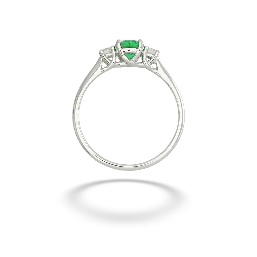 A silver ring featuring a central green heart-shaped emerald-cut gemstone and two small clear accent stones on either side, shown against a plain white background with a soft shadow below. Emerald and Diamond Ring