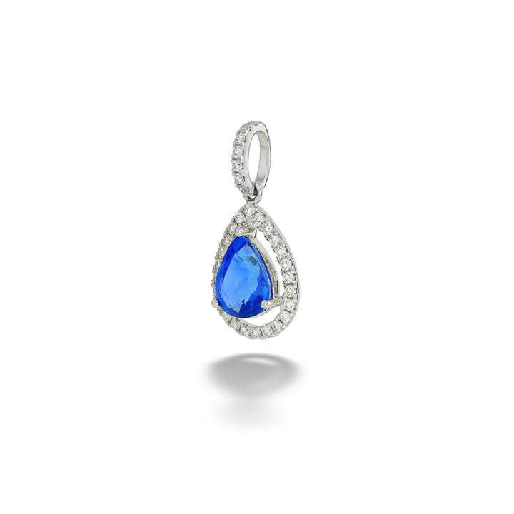 A teardrop-shaped pendant featuring a vibrant blue gemstone surrounded by a halo of small clear stones in a silver-toned setting, shown on a clean white background with a soft shadow below. Pear-Shape Blue Sapphire and Diamond Pendant