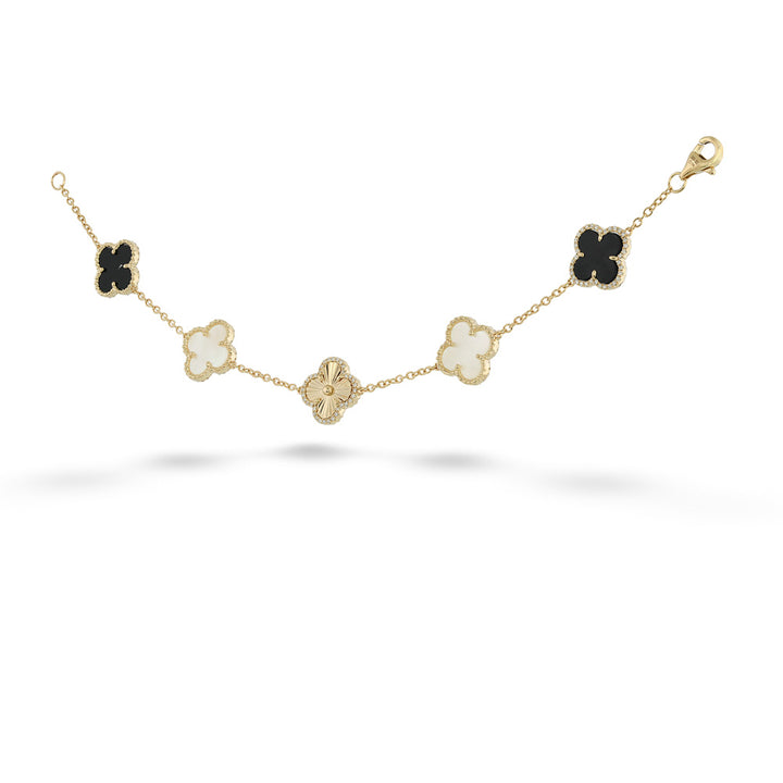A gold chain bracelet featuring five clover motifs in different colors: three black, one milky white, and one gold. The center clover is paved with small clear stones. angled.