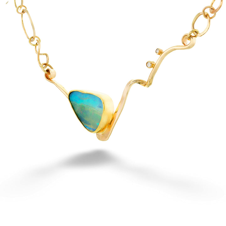 A gold necklace featuring a wavy, organic-shaped pendant with a bezel-set triangular opal stone showing vibrant blue and green play-of-color, suspended from a delicate gold chain on a white background. Opal and Diamond Abstract Chain Necklace by Katrin Wolf 